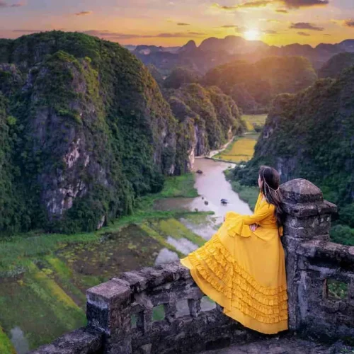 1.-Woman-in-a-yellow-dress-enjoying-the-view-from-a-stone-lookout-at-Mua-Cave-with-a-valley-below-500x500 1.-Woman-in-a-yellow-dress-enjoying-the-view-from-a-stone-lookout-at-Mua-Cave-with-a-valley-below-500x500